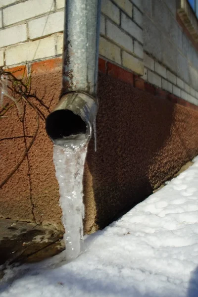 Drainpipe à l'angle de la maison avec de la glace et de la neige sur le sol . — Photo