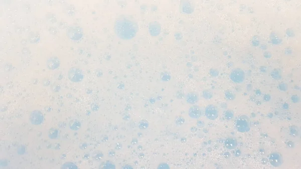Mousse blanche avec petites bulles éclatant dans l'eau bleue — Photo