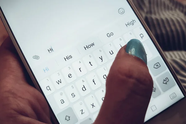La mano femenina con uñas azules está escribiendo en un teléfono inteligente blanco un mensaje hola . — Foto de Stock