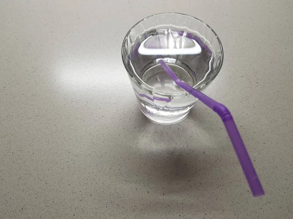 Vaso de agua con tubo de bebida púrpura sobre una mesa de mármol — Foto de Stock