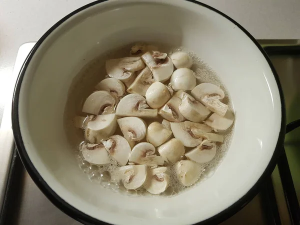 Champinhons fatiados fervidos em água fervida em uma tigela esmaltada . — Fotografia de Stock