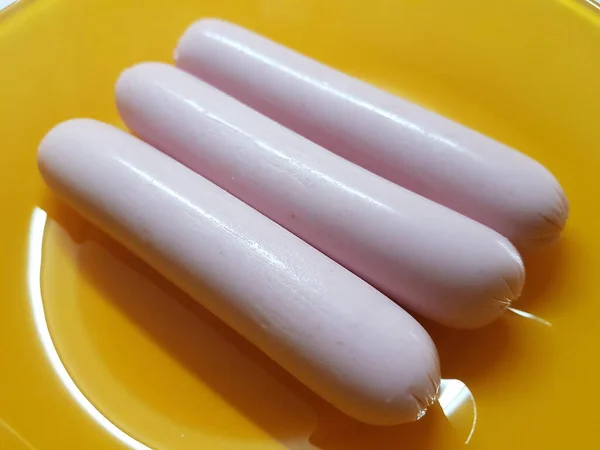 Three raw pink sausages lie in an orange plate — Stock Photo, Image