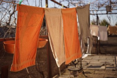 Turuncu banyo havluları ve çizgili bir gömlek, güneşli bahçede çamaşır mandallarıyla bir iple kurutulur..