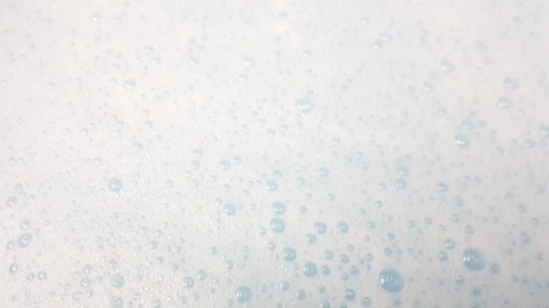 Λευκός αφρός με φυσαλίδες που ξεπροβάλλουν σε μπλε νερό closeup. — Αρχείο Βίντεο