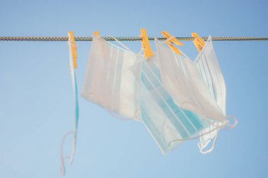 Mavi arka planda sarı mandallı çamaşır ipinde asılı tıbbi yüz maskeleri.