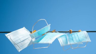 Çamaşır ipinde mandallarla asılı tıbbi yüz maskeleri. Mavi gökyüzü arkaplanı