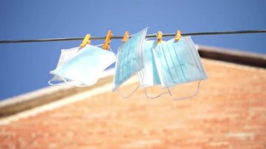Tıbbi maskeler çamaşır ipine mandallarla tutunur. Çatı ve mavi gökyüzü arka planı. Rüzgarlı güneşli bir gün