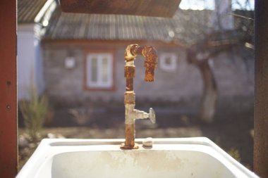 Old rusty faucet on a sink in a rural yard. The facade of the house in the background in blur. Sunny day clipart