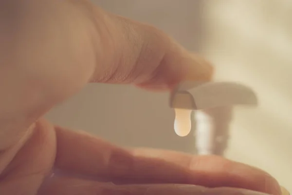 Female finger touch on a liquid soap dispenser. White gel fall out of the bottle.