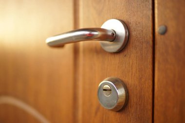 Krom sapı ve anahtar deliği olan parlak, kahverengi ahşap kapı.