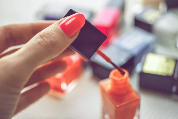 女性手握刷与红色指甲油 一张桌子 上面有一堆不同颜色的指甲油 模糊不清 — 图库照片