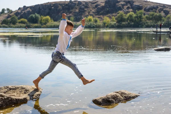 Ung dreng springer fra rock til rock - Stock-foto