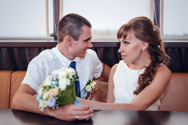 Los recién casados sonrientes se sientan en la cabina de la esquina por las ventanas — Foto de Stock