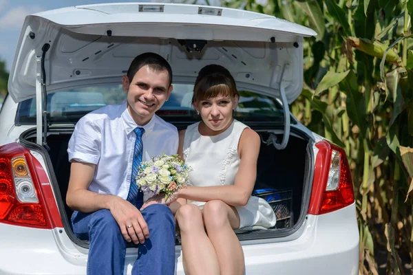 Jeunes mariés assis dans le coffre de la voiture ouverte — Photo