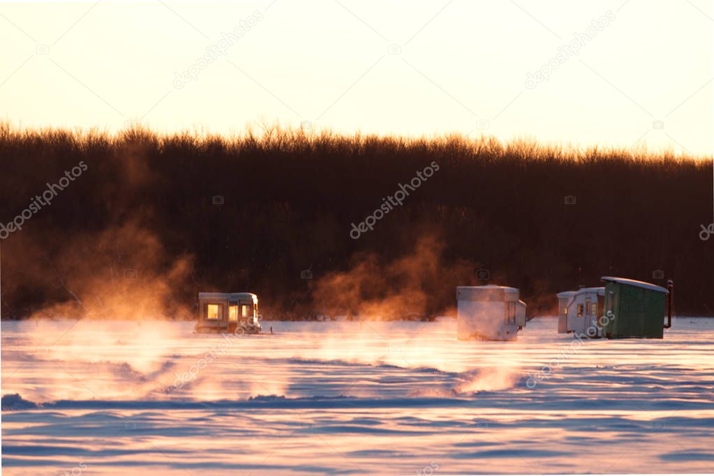 Vapor coming out of the lake where it's not completely frozen, while ice fishing huts are already installed on the lake.