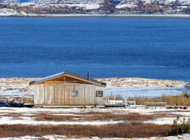 Sonbaharda Nunavik 'teki mavi suların yanındaki ahşap kulübe.