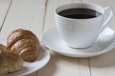 Bir fincan kahve, croisant ve ahşap zemin üzerine ekmek
