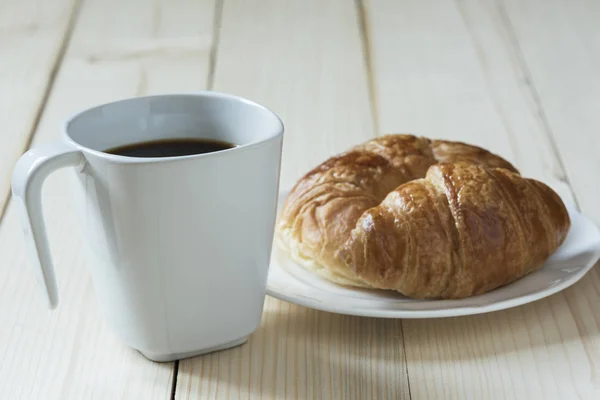 Una taza de café y un pan sobre fondo de madera — Foto de Stock