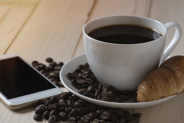 Una taza blanca de café, croissant y smartphone — Foto de Stock