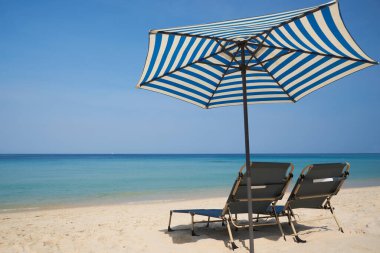 İki plaj sandalyesi ve kumsalda bir şemsiye ve güneşli bir günde mavi deniz.