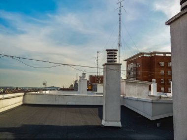 Mavi bir yaz gökyüzü olan şehir manzarası. Bir sürü bacası ve antenleri olan bir çatıdan manzaralar..