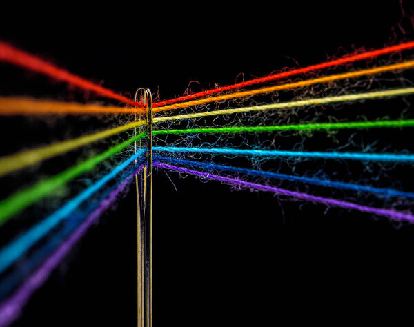 Multicolored threads, forming the colors of the rainbow, are threaded through the eye of a sewing needle, macro