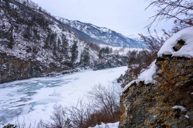Karla kaplı dağlar ve donmuş bir dağ nehri olan bir manzara.