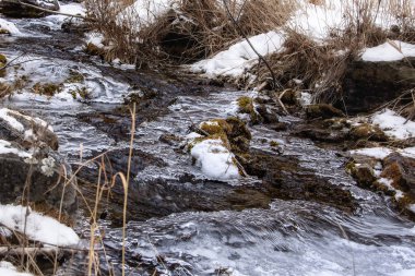Küçük bir dere kışın kayalar arasında akar, kısmen ince buzla kaplıdır.