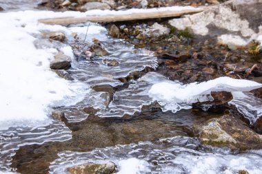 Küçük bir dere kışın kayalar arasında akar, kısmen ince buzla kaplıdır.