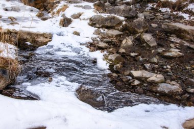 Küçük bir dere kışın kayalar arasında akar, kısmen ince buzla kaplıdır.