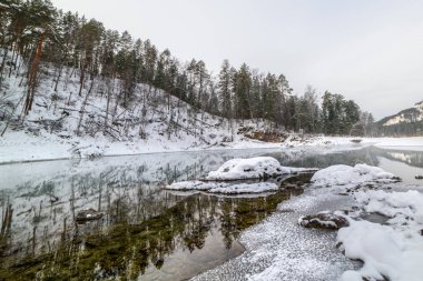 Kışın karla kaplı dağlar ve ağaçların arasında donmamış güzel dağ gölü. Sudaki yansıma.
