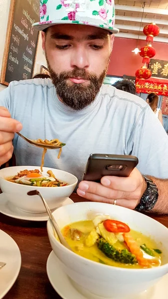 Bearded tourist checking his mobile phone while eating — Stock Photo, Image