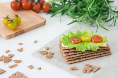 Siyah gevrek ekmek (İsveç kraker) yumuşak peynir, marul izni, kiraz domates ve beyaz zemin üzerine biberiye