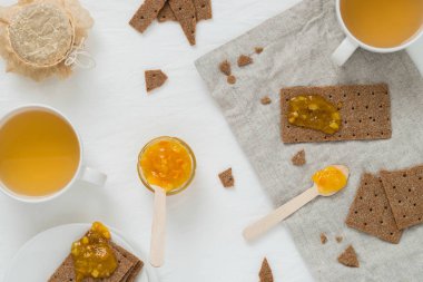 Tatlı yiyecek ya da kahvaltı ile çavdar gevrek ekmek (İsveç kraker), yaymak portakal reçeli, bardak yeşil çay, portakal reçeli Cam Kavanoz, kurutulmuş çiçekler, beyaz arka planda, üstten görünüm