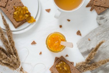 Tatlı yiyecek ya da siyah gevrek ekmek (İsveç kraker), forma portakal reçeli, fincan yeşil çay ile Kahvaltı, reçeli Cam Kavanoz, kurutulmuş çiçekler, beyaz arka planda, üstten görünüm
