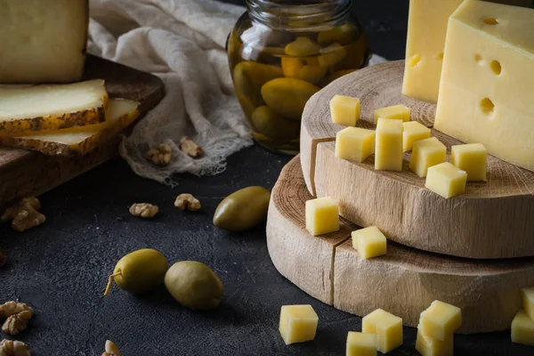 Cheese platter of chopped Swedish hard cheese and sliced and Italian pecorino toscano on wooden boards, with green olives in glass jar and walnuts — Stock Photo, Image