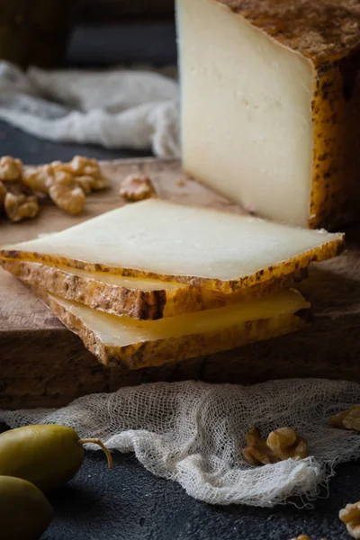 Italian hard cheese pecorino toscano sliced on wooden board with green olives and walnuts — Stock Photo, Image