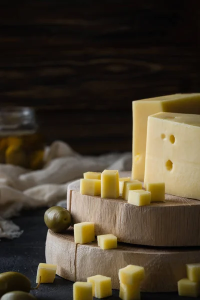 Σουηδική σκληρό κίτρινο τυρί με τρύπες κομμένα στις ξύλινες τάβλες με πράσινες ελιές σε γυάλινο βάζο και καρύδια — Φωτογραφία Αρχείου