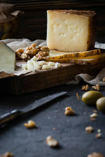 Πιατέλα τυριών από ψιλοκομμένο Ισπανικά σκληρό τυρί manchego και φέτες ιταλικού pecorino toscano σε ξύλινη σανίδα, με πράσινες ελιές σε γυάλινο βάζο και καρύδια — Φωτογραφία Αρχείου