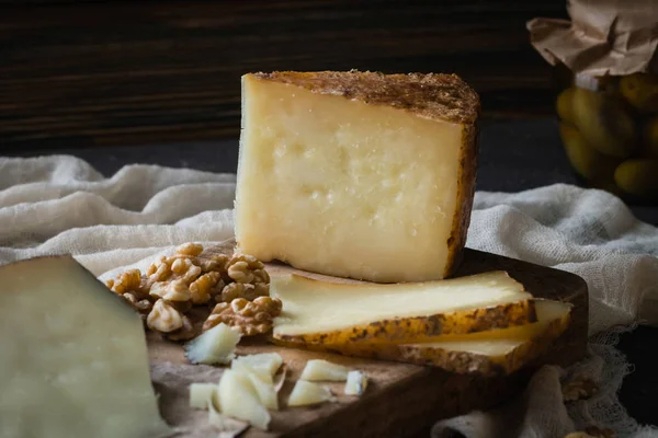 Cheese platter of chopped Spanish hard cheese manchego and sliced Italian pecorino toscano on wooden board, with green olives in glass jar and walnuts — Stock Photo, Image