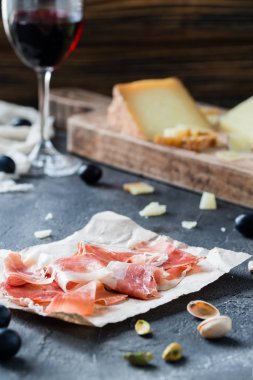 Jambon jamon serrano veya prosciutto crudo ile dilimlenmiş sert peynirler (İtalyan pecorino toscano ve İspanyol manchego), kırmızı şarap ile üzüm, fıstık, rustik koyu arka plan üzerinde