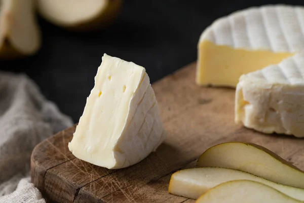 Closeup γαλλικό μαλακό τυρί από την περιοχή της Νορμανδίας φέτες με αχλάδι σε ένα ξύλινο ταμπλό σε σκούρο φόντο για ρουστίκ — Φωτογραφία Αρχείου