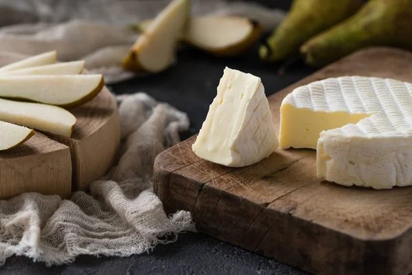 French soft cheese from Normandy region sliced with pear on a wooden board on dark rustic background — Stock Photo, Image