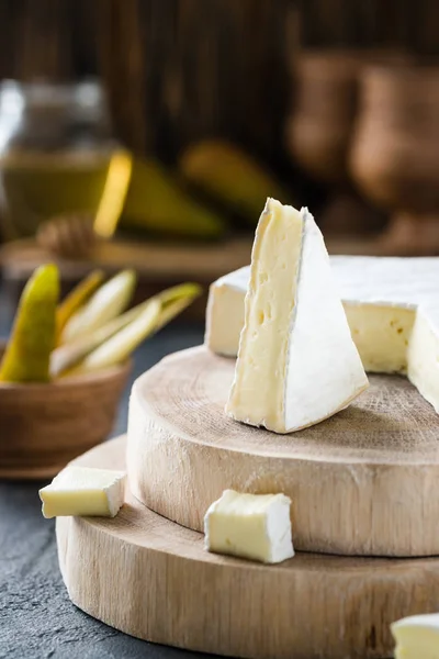 Soft cheese brie sliced on wooden cuts with honey and pear on dark rustic background — Stock Photo, Image