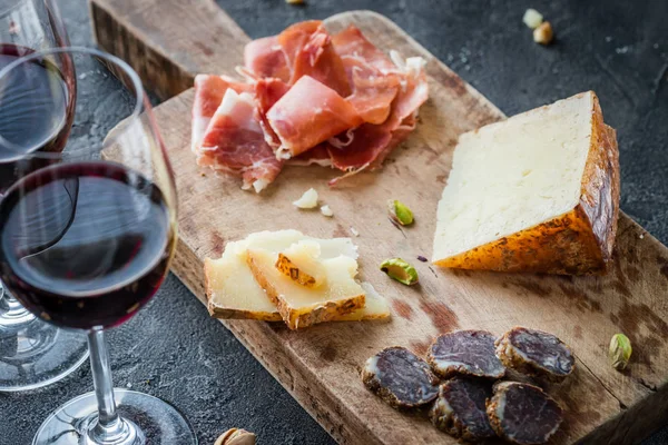 İspanyolca jambon jamon serrano veya İtalyan prosciutto crudo, birlikte dilimlenmiş İtalyan sert peynir pecorino toscano, ev yapımı kurutulmuş et salam, bardak kırmızı şarap ve antep fıstığı, eski ahşap tahta üzerinde