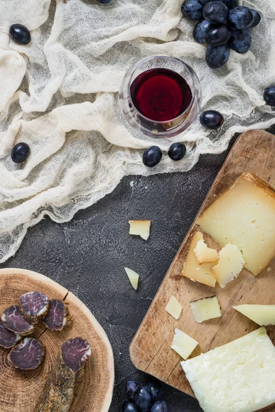 Birlikte sert peynirler (İtalyan pecorino toscano ve İspanyol manchego) ve ev yapımı kurutulmuş et, bardak kırmızı şarap üzüm ile rustik koyu arka plan üzerinde Üstten Görünüm