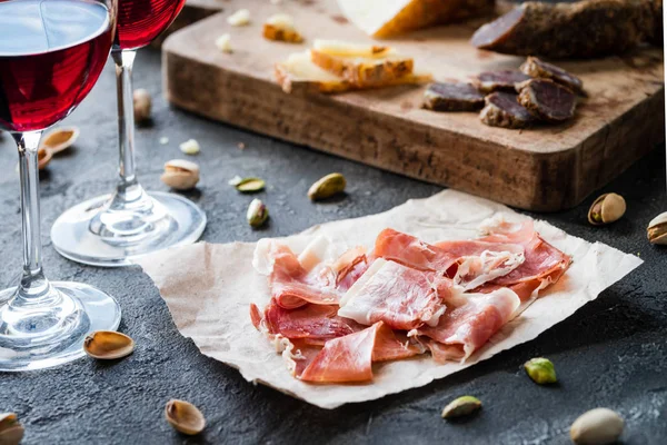 Jamon serrano veya dilimlenmiş İtalyan sert peynir pecorino toscano, ev yapımı kurutulmuş et salam, kırmızı şarap ve antep fıstığı, rustik koyu arka plan üzerine gözlük ile İtalyan prosciutto crudo İspanyolca jambon