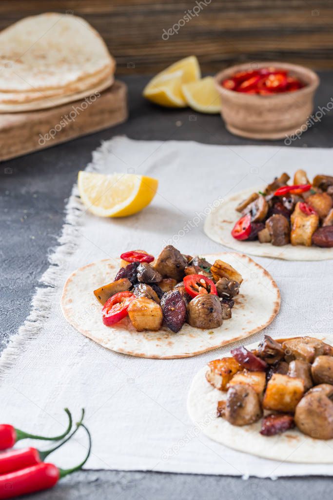 Tacos with grilled mushrooms, Spanish spicy sausage chorizo, Mexican tortillas, Cypriot cheese halloumi, hot chilly, dried oregano, slices of lime and lemon, on cloth