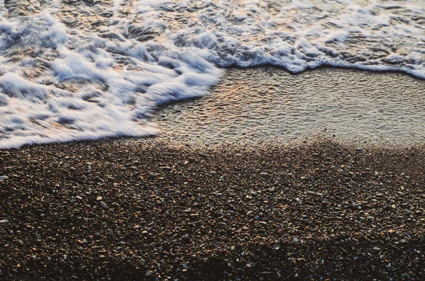 Eine blubbernde Welle in Bewegung auf nassen kleinen Kieselsteinen — Stockfoto