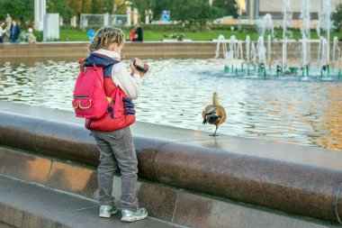 Kız, parkta fıskiyenin yanında ördek resmi çekiyor.